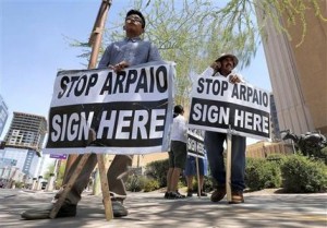 Simón López, izquierda, e Hiliaro Islas sostienen carteles mientras participan en una colecta de firmas para convocar a un referendo revocatorio contra el alguacil del condado Maricopa, Joe Arpaio, el miércoles 29 de mayo de 2013, en el centro de Phoenix, Arizona. Arpaio ha sido acusado de aplicar políticas raciales contra los latinos. (Foto AP/Matt York)