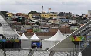 Un grupo de trabajadores termina de instalar una valla en el graderío de la Arena de Sao Paulo, el martes 10 de junio de 2014, a dos días del partido que inaugurará el Mundial. Al fondo se aprecian las casas del suburbio de Itaquerao (AP Foto/Thanassis Stavrakis)