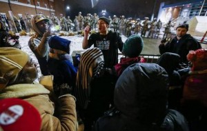 Algunos manifestantes cantan consignas mientras policías y agentes de la Guardia Nacional hacen guardia en la comisaría de Ferguson en Misuri (Estados Unidos) ayer, miércoles 26 de noviembre de 2014. Con un aspecto casi fantasmal, la localidad de Ferguson (EE.UU.) intentó hoy retomar la normalidad, tras dos noches de disturbios por la decisión de un jurado de no imputar al policía blanco que mató a tiros al joven negro Michael Brown. EFE